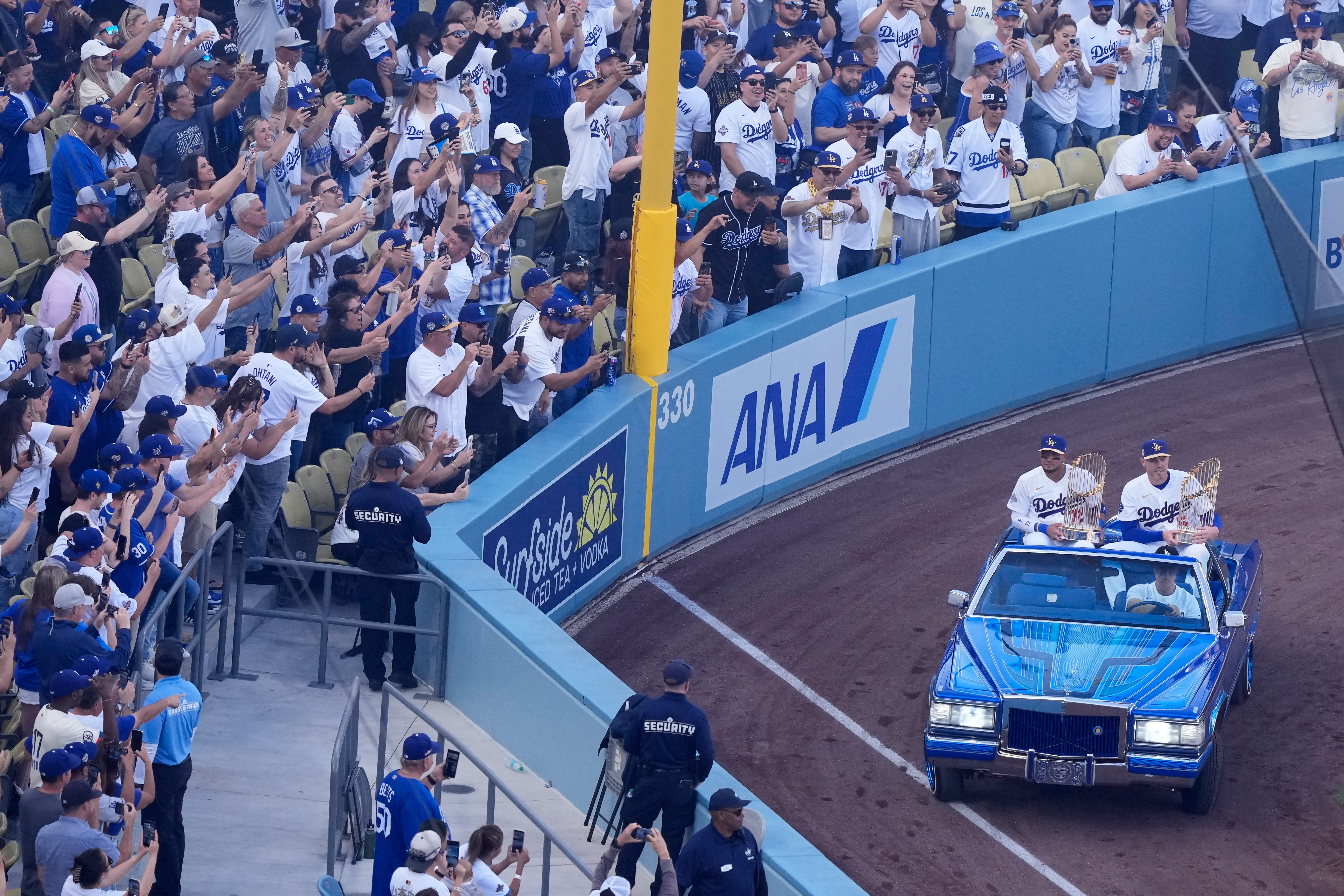 Miguel Rojas y Freddie Freeman cargan los trofeos de las pasadas dos Series Mundiales de los Dodgers mientras son transportados en un auto por el actor Will Ferrell en la ceremonia de apertura de la temporada 2026.